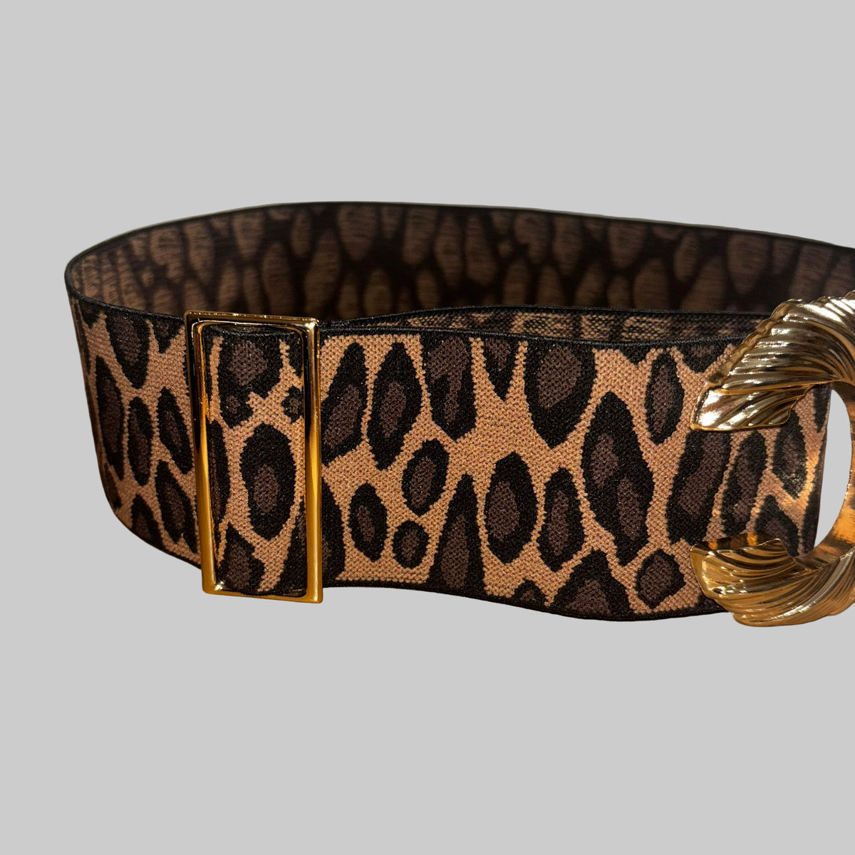 Leopard print belt with a gold buckle on a wooden surface