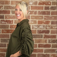 olive green rushed sleeve blouse against a brick wall