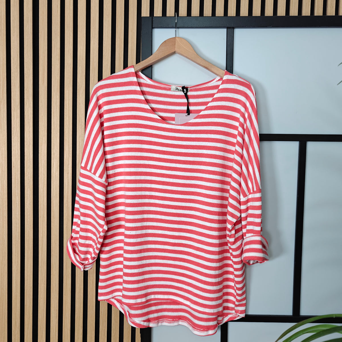 Coral and white striped shirt on a hanger against a striped wall.