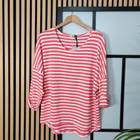 Coral and white striped shirt on a hanger against a striped wall.