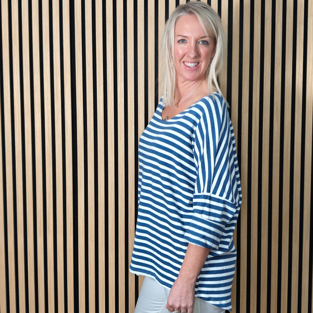 Woman wearing a denim blue and white striped shirt standing against a striped wall.