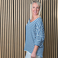 Woman wearing a denim blue and white striped shirt standing against a striped wall.