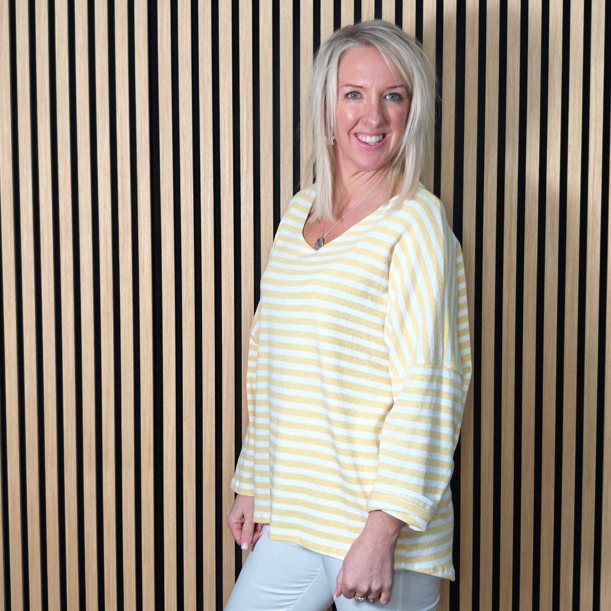 Woman wearing a lemon striped shirt standing against a striped wall.