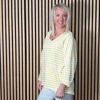 Woman wearing a lemon striped shirt standing against a striped wall.