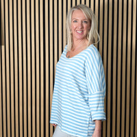 Woman wearing a sky blue and white striped shirt standing against a striped wall.