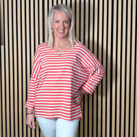 Woman wearing a coral and white striped shirt against a striped wall.