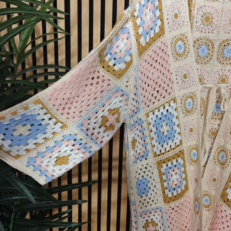 Close-up of a crocheted jacket with floral patterns against a wooden background.