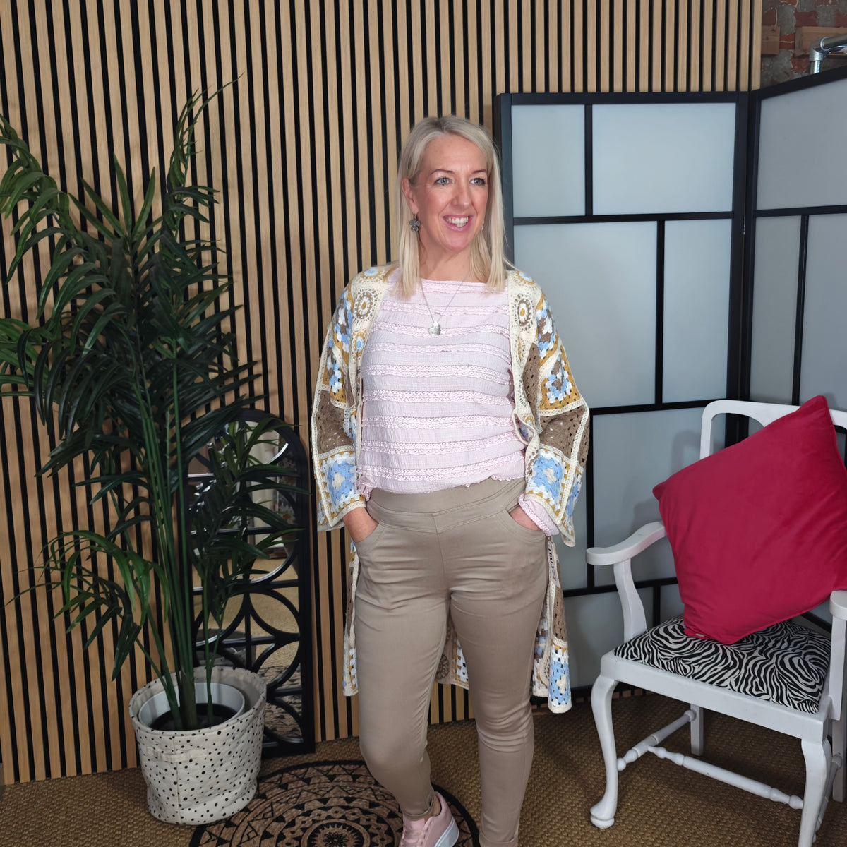 Woman standing in a room with a plant and chair, smiling.