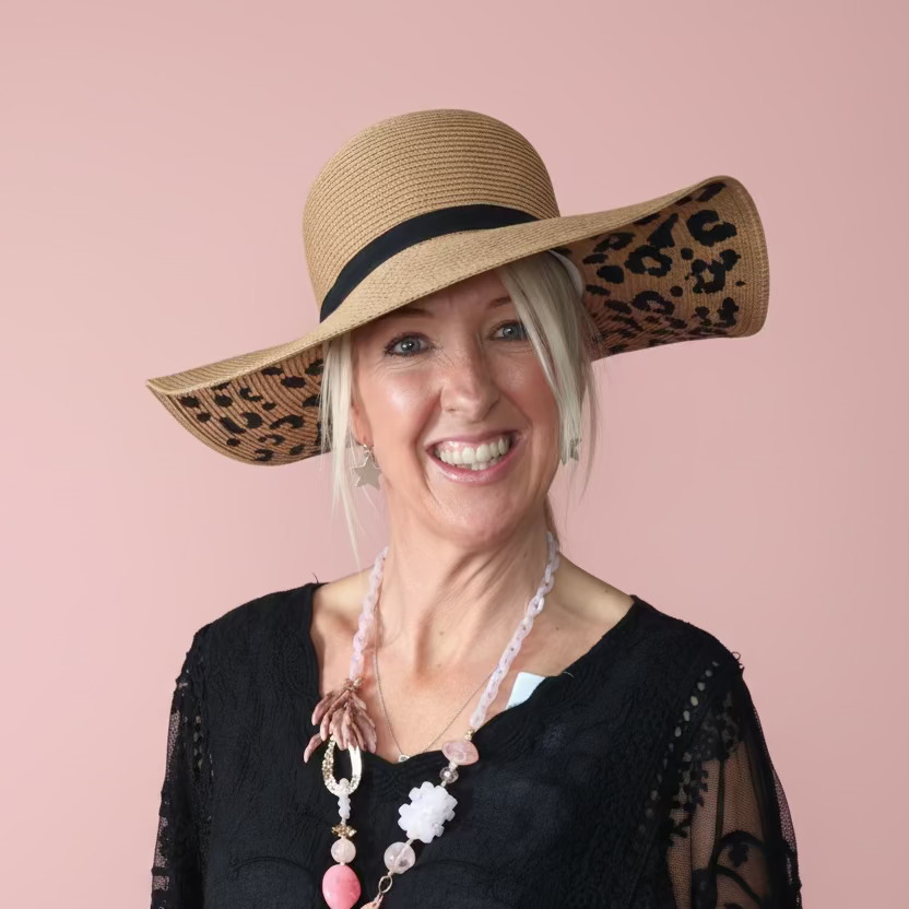 Woman wearing a wide-brimmed hat with leopard print details on a pink background
