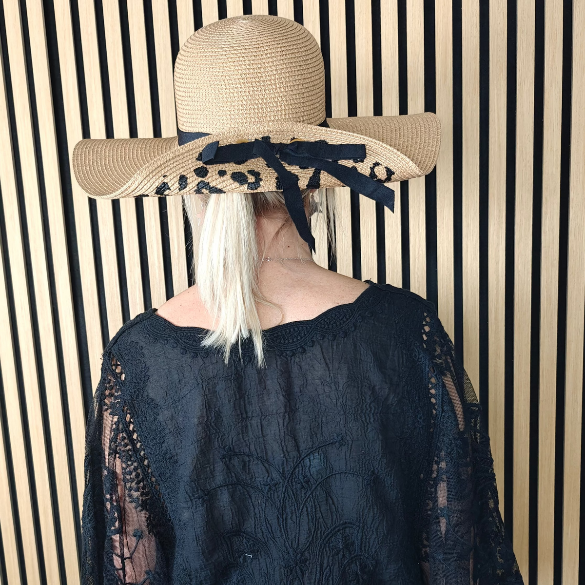 Person wearing a dark blue top with sheer sleeves and a wide-brimmed hat against a striped wall.
