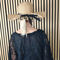 Person wearing a dark blue top with sheer sleeves and a wide-brimmed hat against a striped wall.