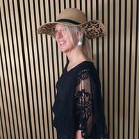 Woman wearing a wide-brimmed hat with leopard print trim against a striped wall.