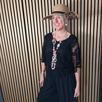 Woman wearing a black outfit and wide-brimmed hat with leopard print trim against a striped wall.