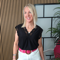 Woman wearing a black top with lace details and white pants, standing indoors.