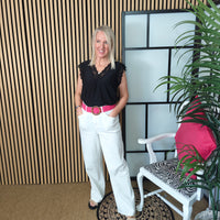 Woman in black top and white pants standing in a room with a striped wall and chair.