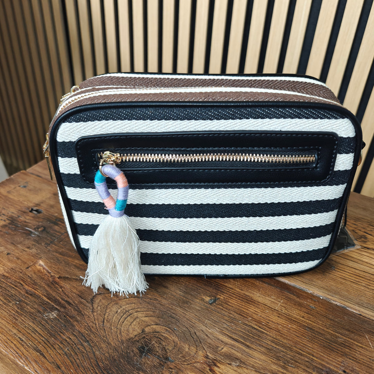 Black and white striped bag with a tassel charm on a wooden surface