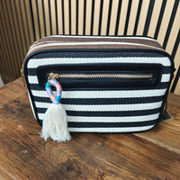 Black and white striped bag with a tassel charm on a wooden surface