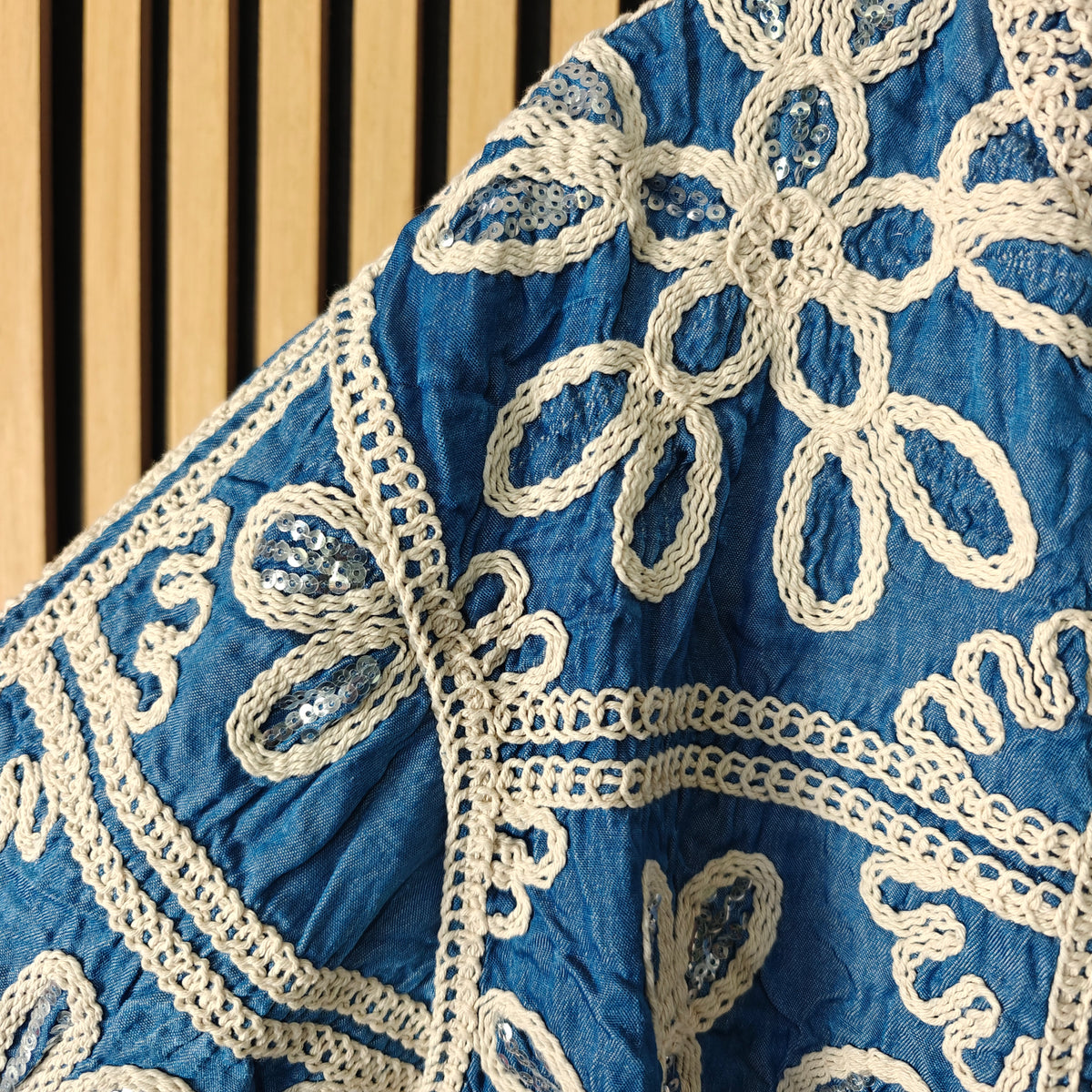 Close-up of a blue fabric with intricate white lace detailing on a wooden surface.