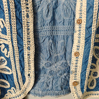 Close-up of blue fabric with intricate white embroidery and beige lace trim.