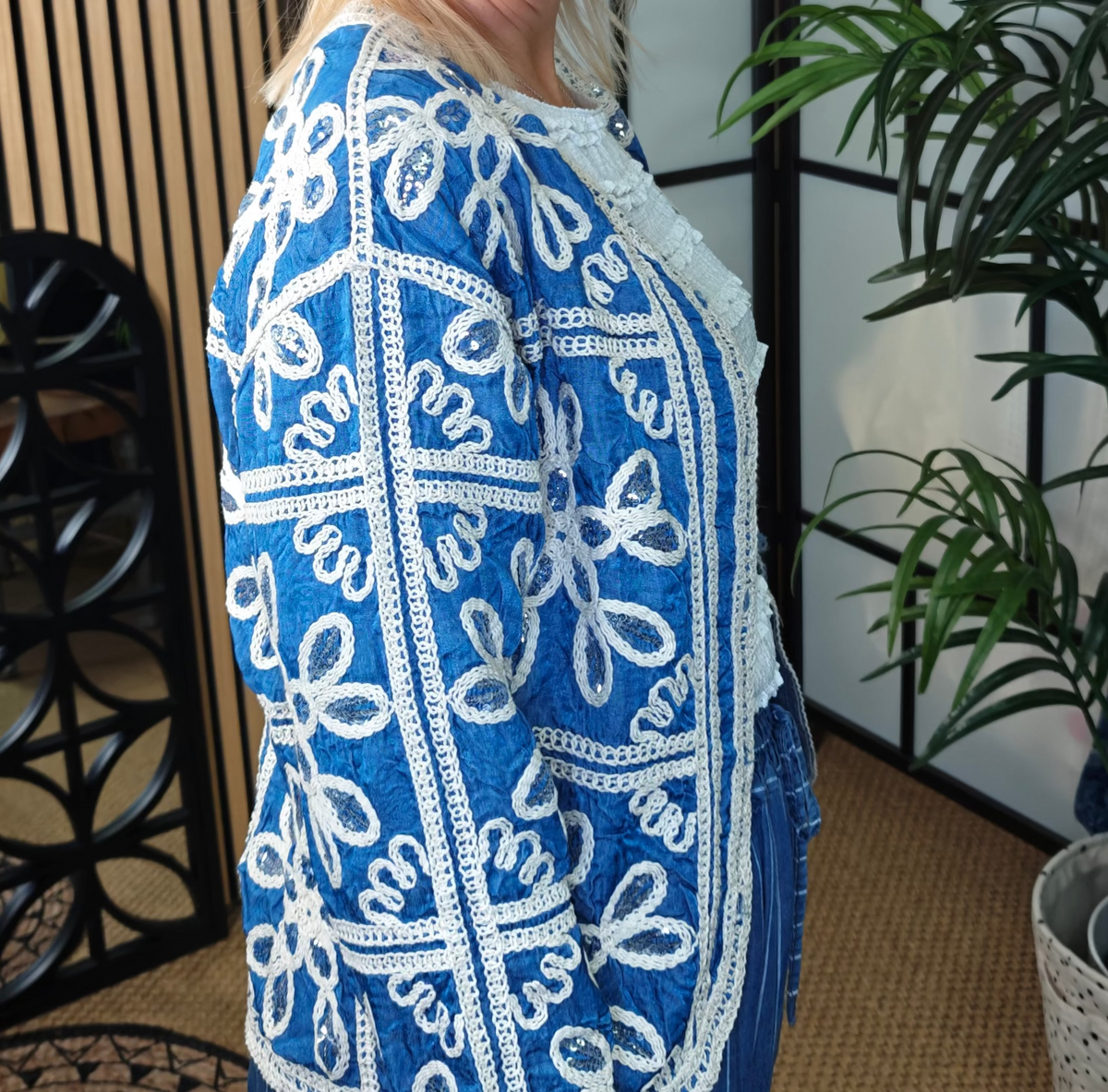 Woman wearing a blue and white patterned top in an indoor setting with plants and decor.