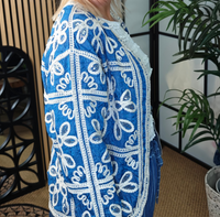 Woman wearing a blue and white patterned top in an indoor setting with plants and decor.