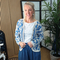 Woman wearing a blue and white patterned cardigan in an indoor setting with plants.
