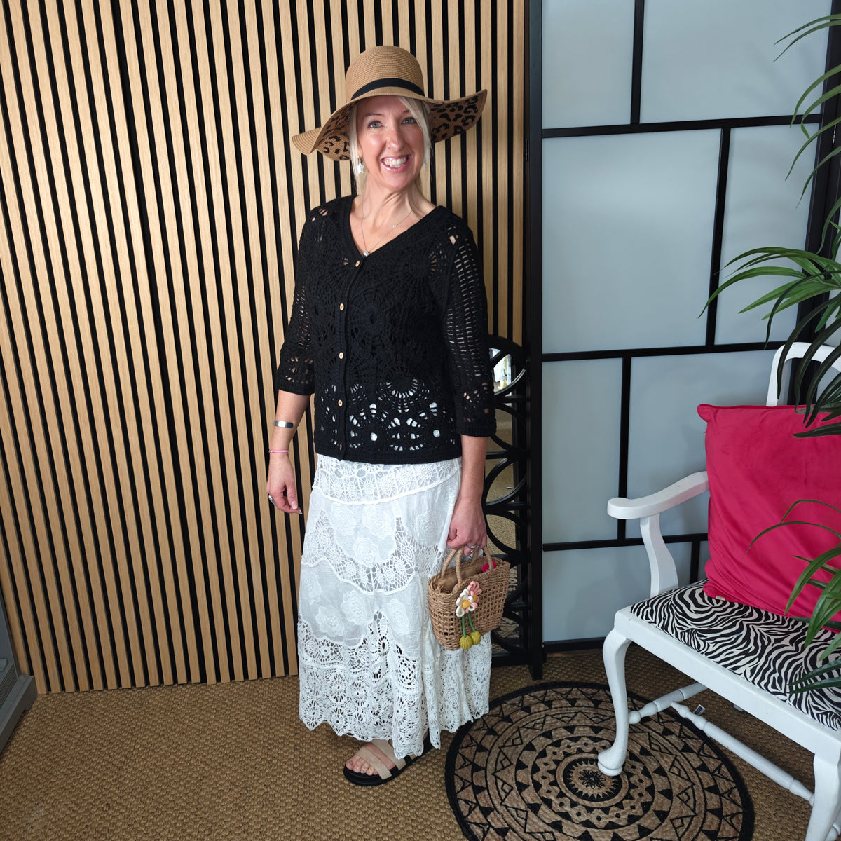 Woman wearing a black top and white lace skirt with a straw hat, standing indoors.