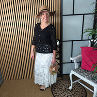 Woman wearing a black top and white lace skirt with a straw hat, standing indoors.