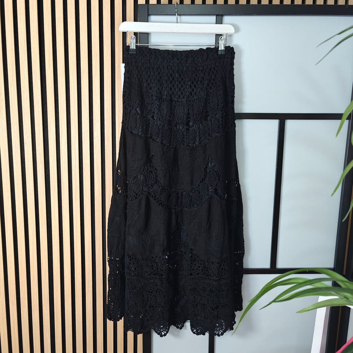 Black lace dress hanging on a rack against a striped wall.