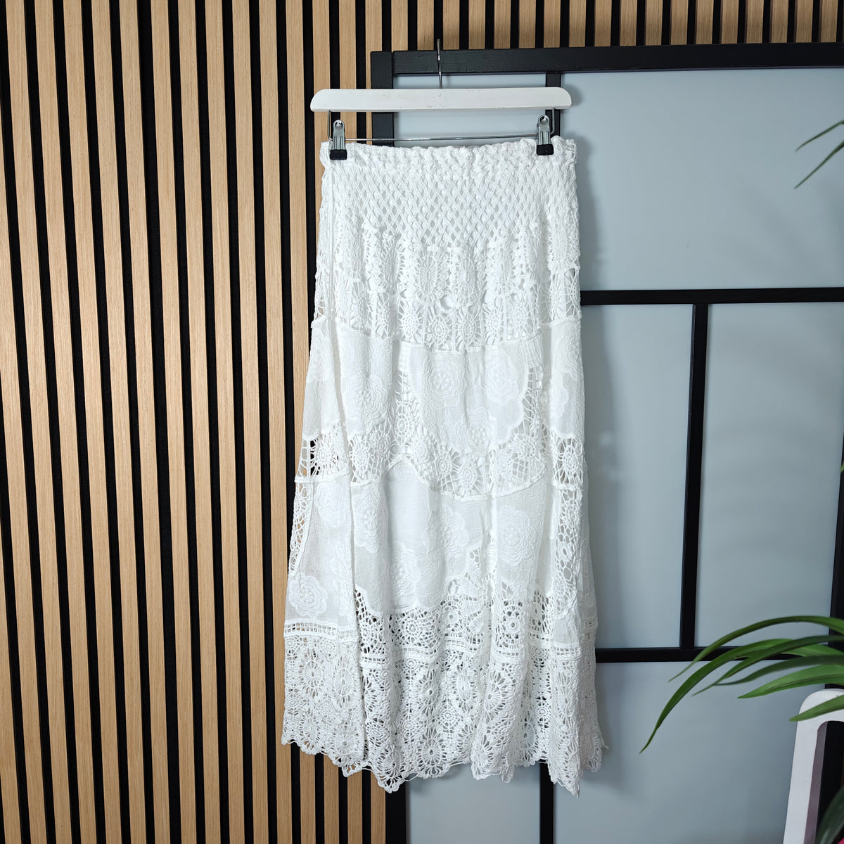 White lace skirt on a hanger against a striped wall.