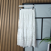 White lace skirt on a hanger against a striped wall.