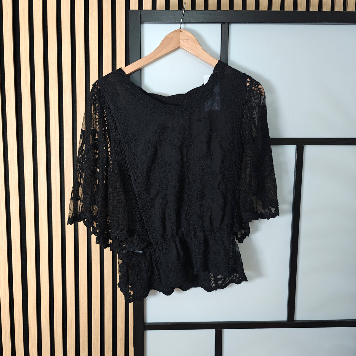 Black lace top on a hanger against a striped wall.