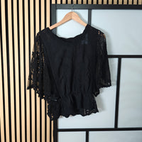 Black lace top on a hanger against a striped wall.