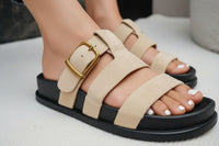 Beige sandals with black soles worn with blue jeans on a light background