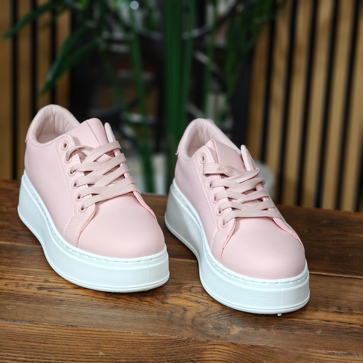 Pair of pink sneakers with white soles on a wooden surface.