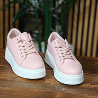Pair of pink sneakers with white soles on a wooden surface.
