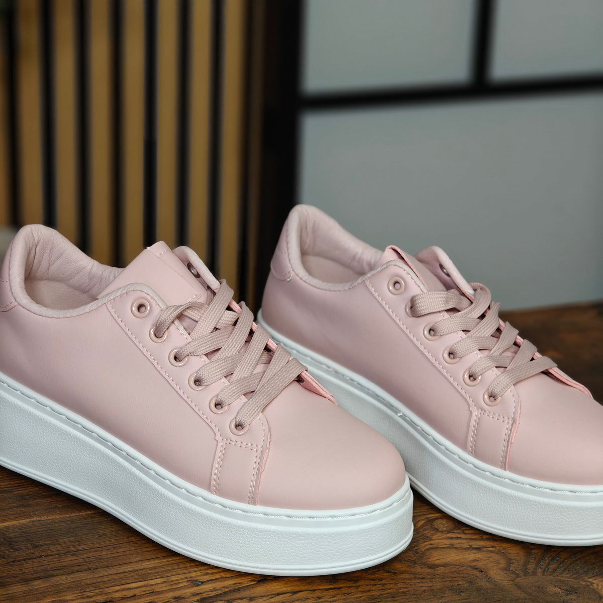 Pair of pink sneakers with white soles on a wooden surface.