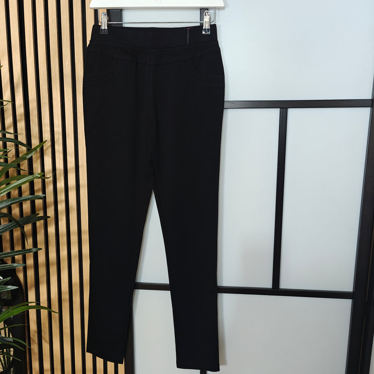 Black pants hanging on a rack against a light background