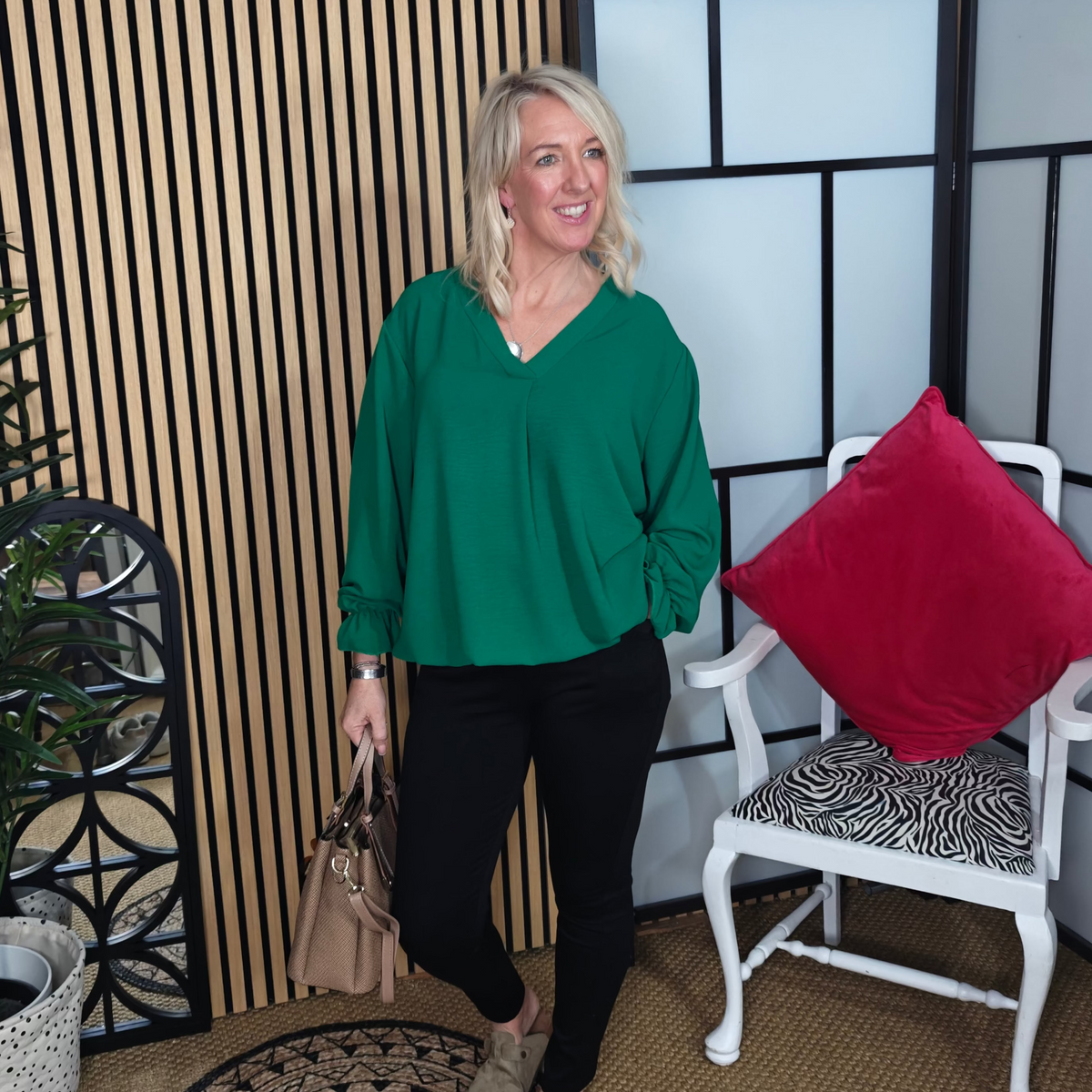 Woman in a green top standing in a room with a chair and decorative elements.