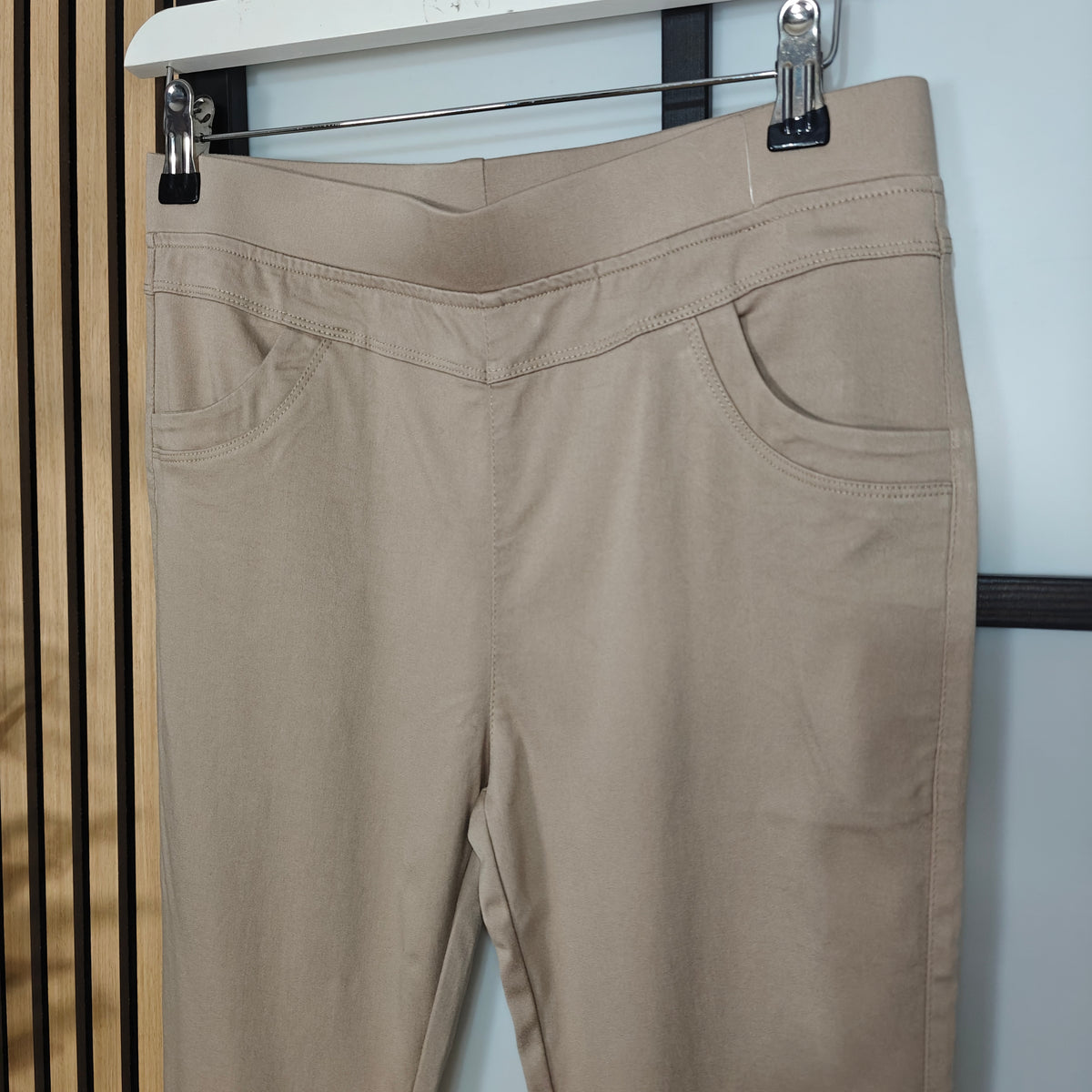 Beige pants hanging on a rack against a white wall.