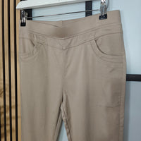 Beige pants hanging on a rack against a white wall.