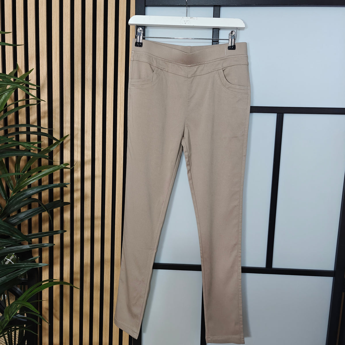 Beige pants hanging on a rack against a striped wall.