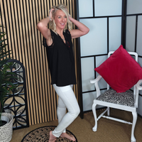 Woman posing in a room with a plant, decorative wall, and chair with a red pillow.