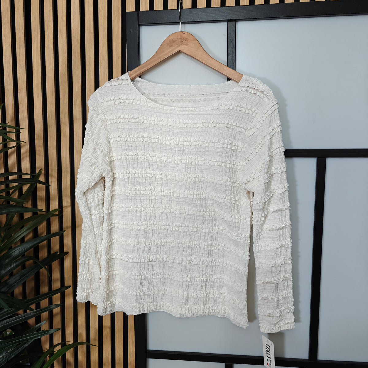White textured sweater on a wooden hanger against a neutral background