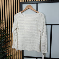 White textured sweater on a wooden hanger against a neutral background