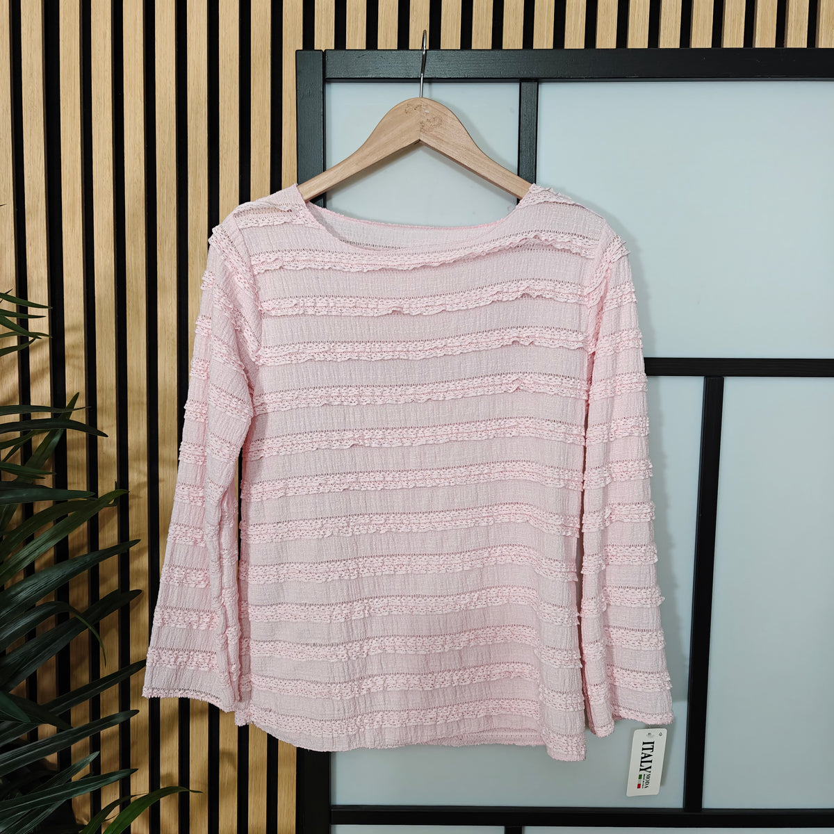 Pink textured sweater on a hanger against a light blue wall with black frames.