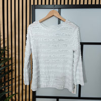 White textured sweater on a hanger against a neutral background