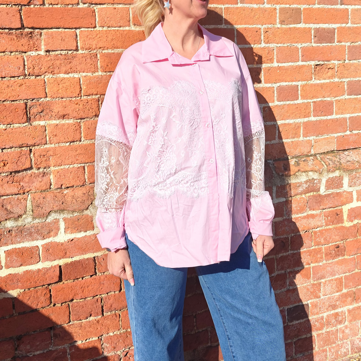 Woman wearing a pink blouse and sunglasses standing against a brick wall.
