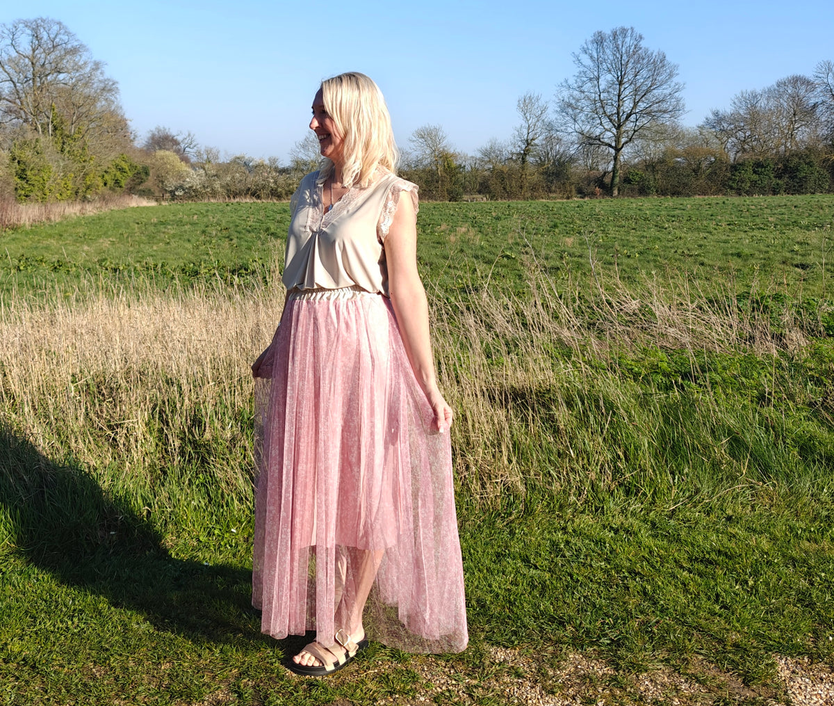 Woman in a white top and pink skirt standing in a field with trees in the background