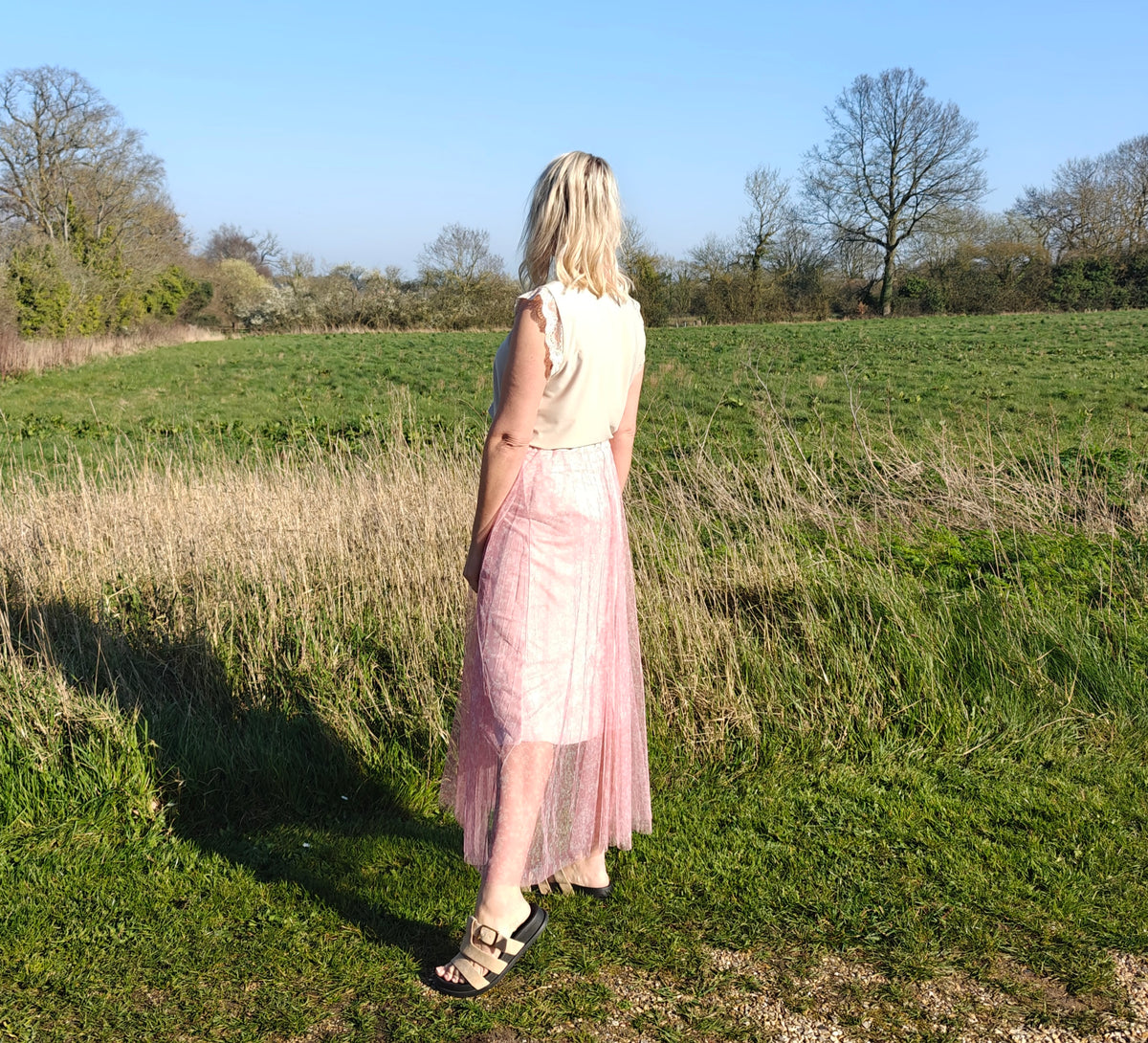 Woman in a pink dress standing in a field with trees in the background